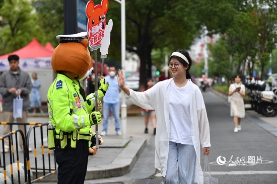 6月7日上午9時，隨著鈴聲的響起，2023年江西高考正式開考，江西省的53.57萬考生以縣（區(qū)）為單位隨機安排在全省256個考點、18968個考場參加高考。圖為“小熊交警”和考生擊掌鼓勵。 人民網(wǎng)記者 時雨攝