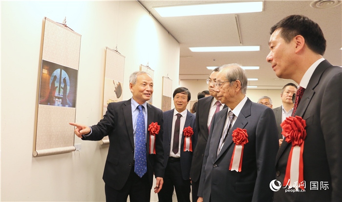 “湖州印象”攝影展主創(chuàng)、世界華人攝影協(xié)會副會長馮學(xué)敏向吳江浩大使、福田康夫前首相等嘉賓介紹展出作品。（人民網(wǎng) 許可攝）