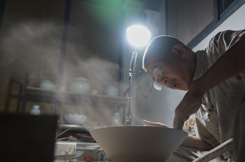 ↑ 在景德鎮(zhèn)，手工匠人吹去坯內(nèi)的泥土（2021年7月14日攝）。