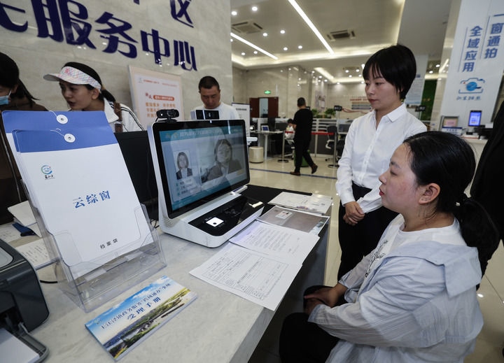 在浙江省嘉興市秀洲區(qū)王江涇鎮(zhèn)便民服務中心的“跨域通辦·云綜窗”窗口，辦理開業(yè)登記的個體工商戶（右一）通過該系統(tǒng)與江蘇省蘇州市吳江區(qū)盛澤鎮(zhèn)行政審批局工作人員視頻連線，進行身份讀取及材料線上審核（2024年5月9日攝）。新華社記者 徐昱 攝