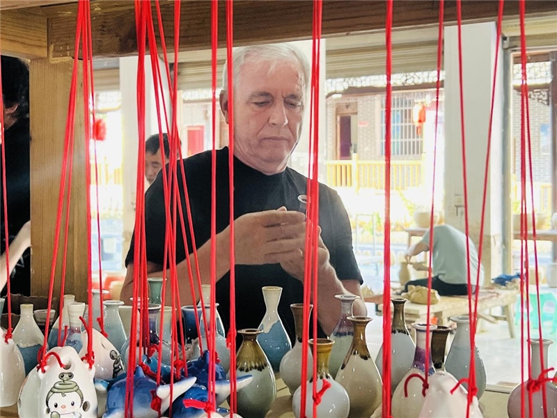 鄉(xiāng)愁如同一根根紅線(xiàn)，將游子與故鄉(xiāng)永遠(yuǎn)地牽連到一起。花茂村陶藝文化創(chuàng)意一條街的母氏陶藝館內(nèi)，紅線(xiàn)吊著陶瓶，思緒游走萬(wàn)里。摩爾多瓦“信息標(biāo)簽”通訊社社長(zhǎng)亞歷山大·塔納斯端詳著館內(nèi)展示的陶藝作品，并挑選出心儀的小擺件帶回摩爾多瓦，也帶走花茂村的“鄉(xiāng)愁”。（張亞欣攝）