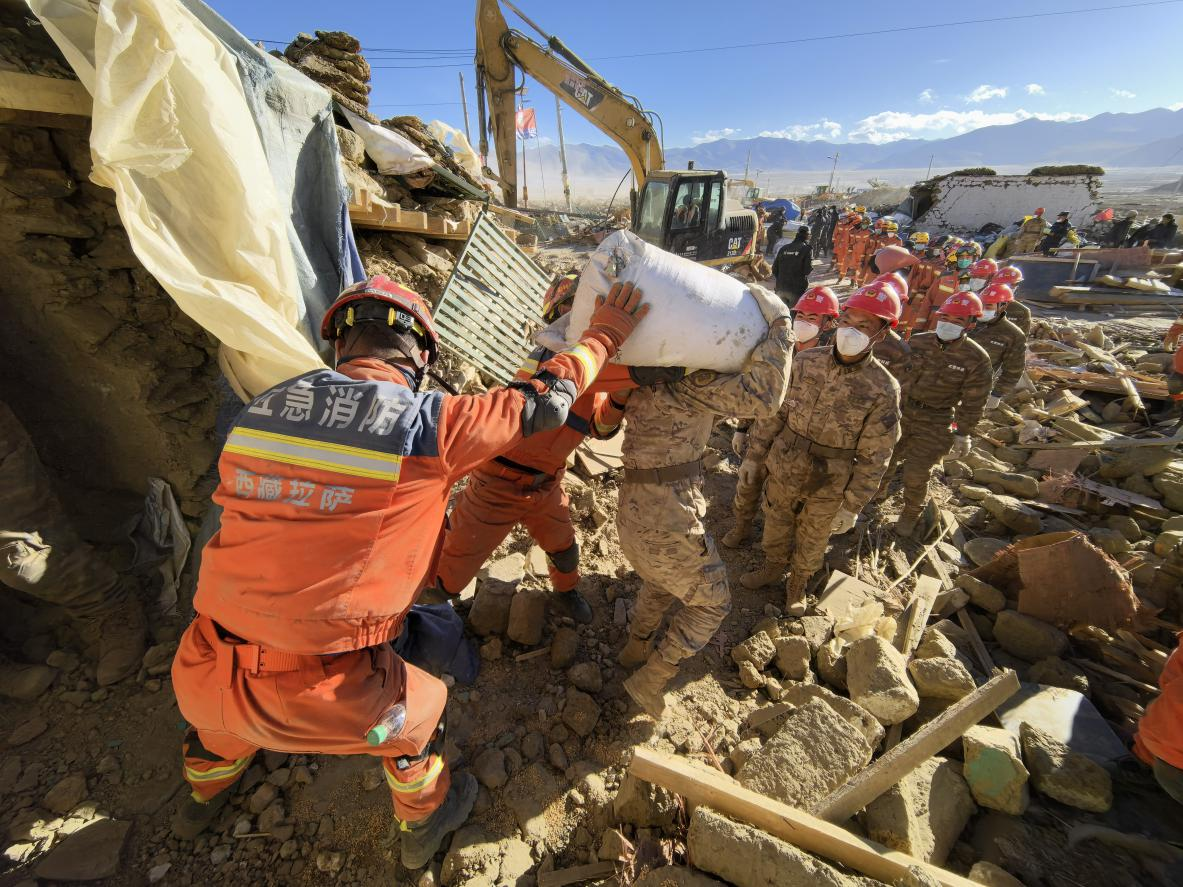 1月11日，定日縣長所鄉(xiāng)古榮村，應急消防等救援人員排隊接力搶運掩埋在倒塌房屋下的群眾財物。人民日報記者楊翹楚攝